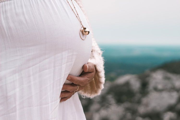 Femme enceinte, les mains posées sur son ventre, face à la campagne