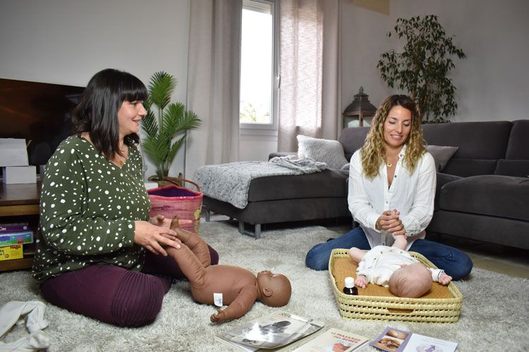 Atelier massage bébé : deux femmes et un bébé installés sur un tapis dans un salon
