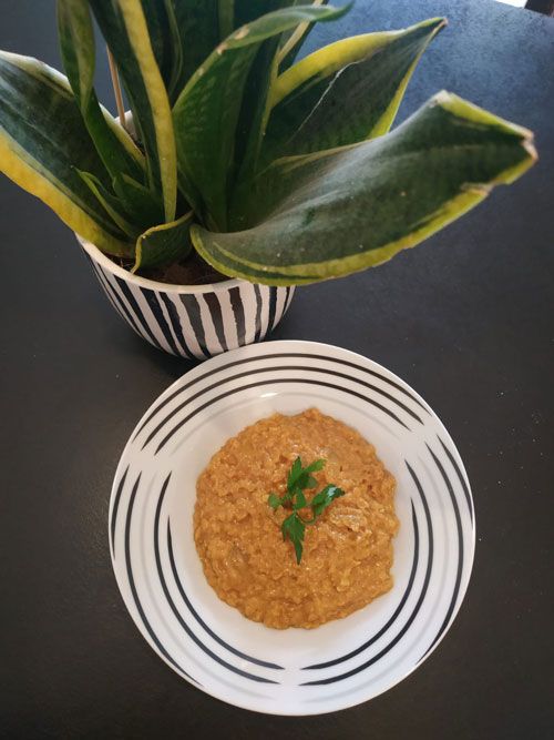 Une assiette de purée orangée garnie d'herbes, près d'une plante verte
