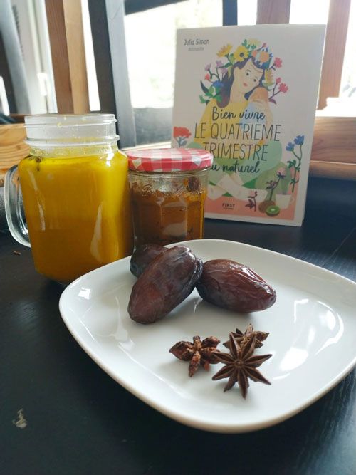Des dattes et de l'anis étoilé dans une assiette, un bocal de jus orangé et un livre