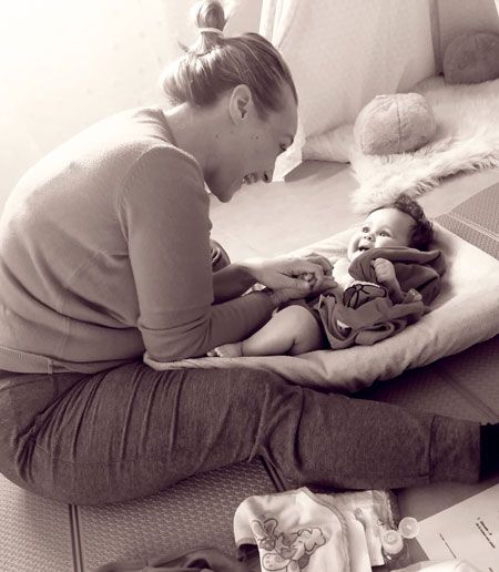 Une maman sourit à son bébé allongé sur un coussin pendant un massage