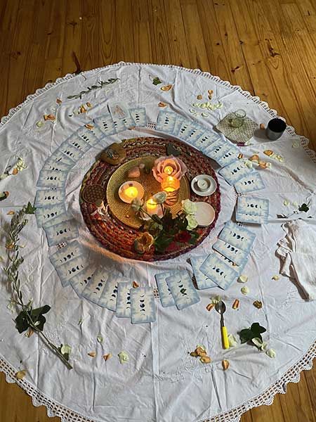 Un cercle de bougies et de petits objets posé sur une nappe blanche, avec des branches de fleurs séchées